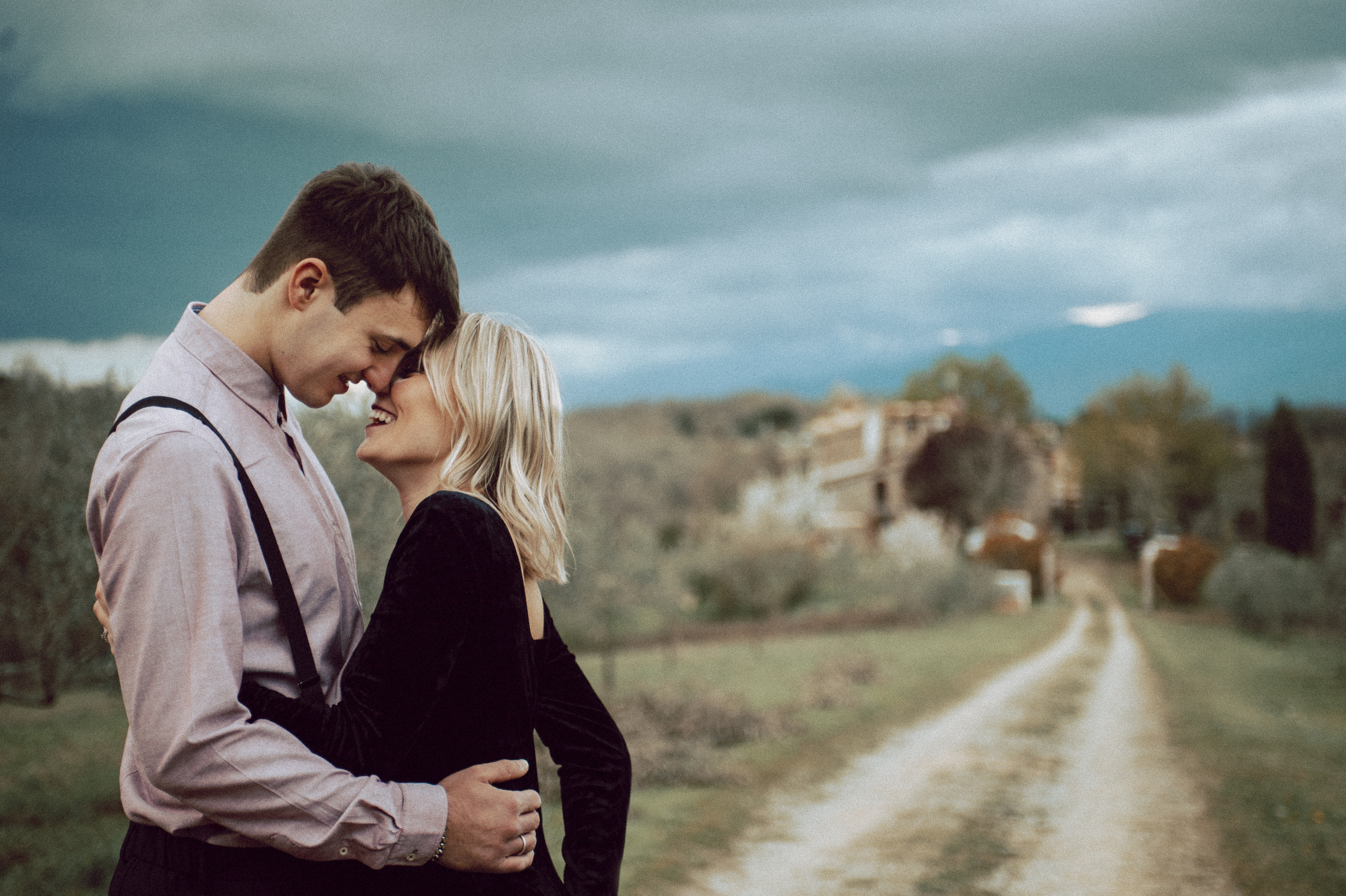 Tuscany Engagement Session - Couple hugging with Tuscany countryside in the background