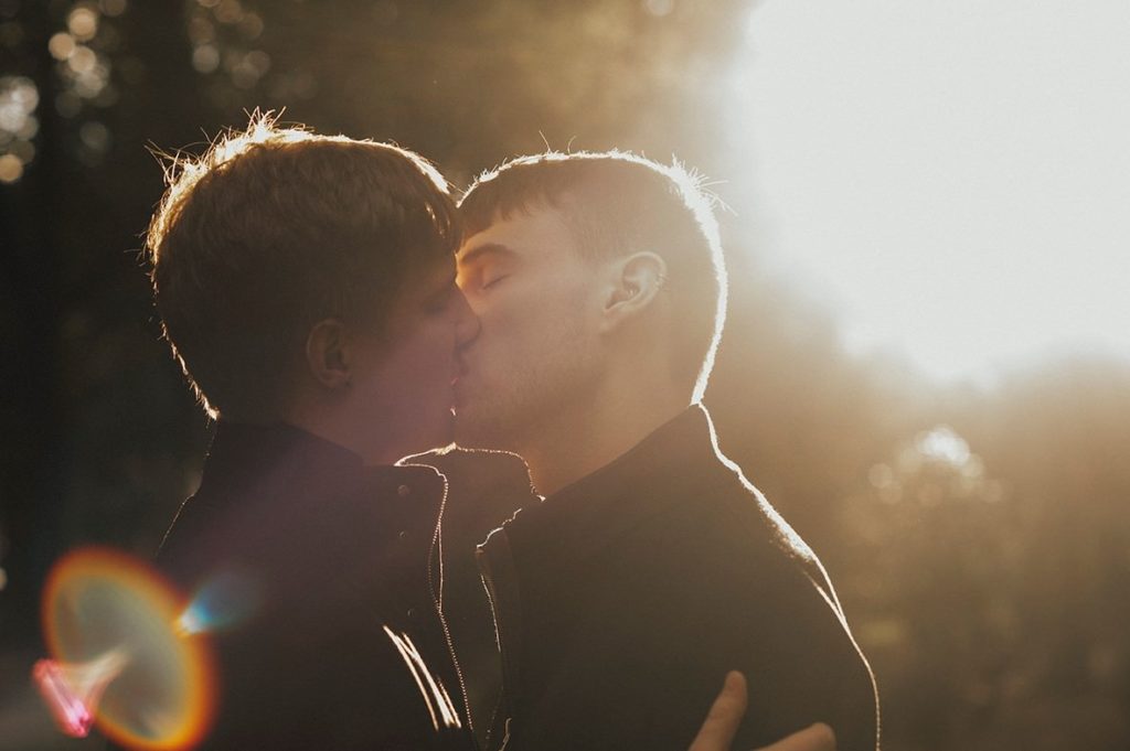 Gay couple kissing with a strong dawn light and a rainbow flare
